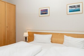Ein Hotelzimmer mit Bett, einem Holzschrank, einem Nachttisch mit Lampe und zwei gerahmten Bildern an der Wand.
