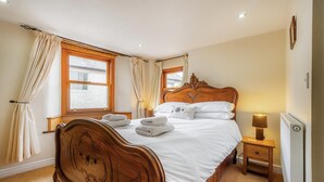 Een slaapkamer met een houten bed, twee nachtkastjes, een raam met gordijnen en een radiator.