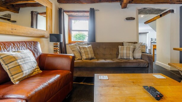 Een gezellige woonkamer met een bruine leren bank, een houten salontafel en een houten plafond met zichtbare balken.