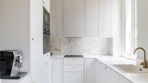 Une cuisine compacte avec des meubles blancs, un pare-feu en marbre, une machine à café et une fenêtre donnant sur un beau paysage.