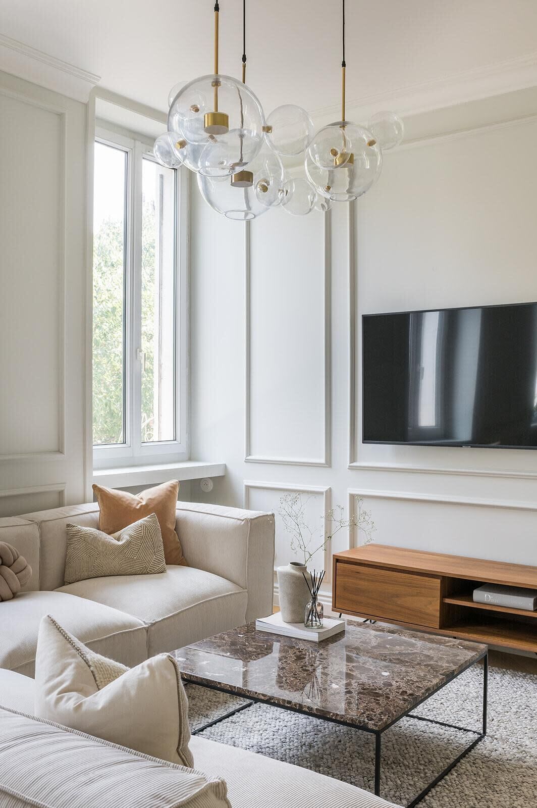 Una sala de estar con sofá, mesa de centro, televisor y un ventanal amplio.