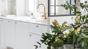 Une cuisine moderne avec des meubles blancs, un robinet doré et une grande fenêtre.