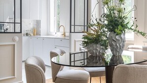 Une cuisine moderne avec des meubles blancs, un coin repas doté d’une table en verre et un luminaire suspendu.