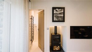 A hallway with a wooden door, a black wood-burning stove, a framed picture on the wall, and a TV mounted on the wall. - 1 Bed in Windermere (oc-lr225) (Windermere)