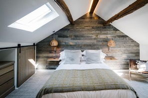 Un dormitorio con techo inclinado, paneles de madera, una cama con almohadas, una mesita de noche y una lámpara colgante.
