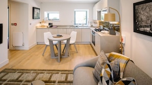 A modern kitchen with white cabinets, a dining table with chairs, and a large window. - 1 Bed in Windermere (oc-lr225) (Windermere)