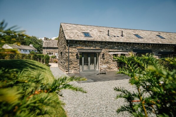 A stone building with a sloped roof, a door, and a small patio area. - 1 Bed in Windermere (oc-lr226) (Windermere)