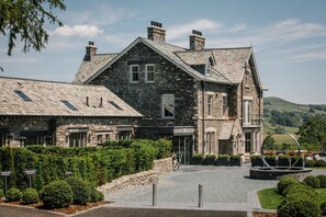 A stone building with a sloped roof, multiple chimneys, and a well-maintained garden. - 1 Bed in Windermere (oc-lr226) (Windermere)