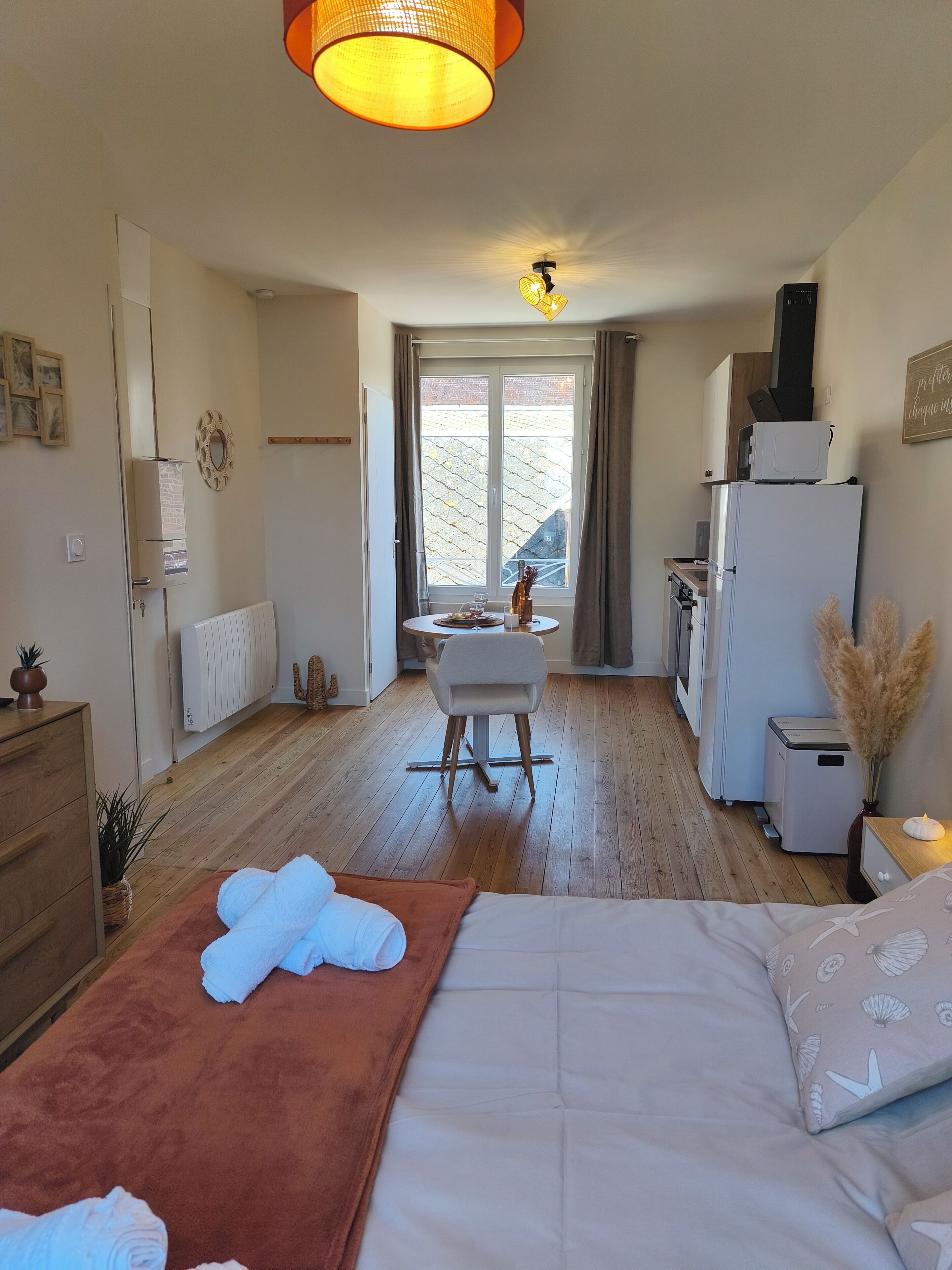 Habitación de hotel con cama, escritorio, silla, radiador, ventana con cortinas y vistas al exterior.