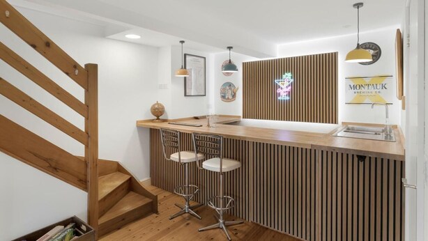 Een keuken met een houten aanrecht, barstoelen, een neonbord en een trap.