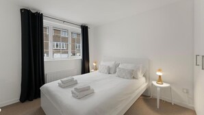 Een hotelkamer met een bed, twee nachtlampjes, een raam met gordijnen en een radiator.