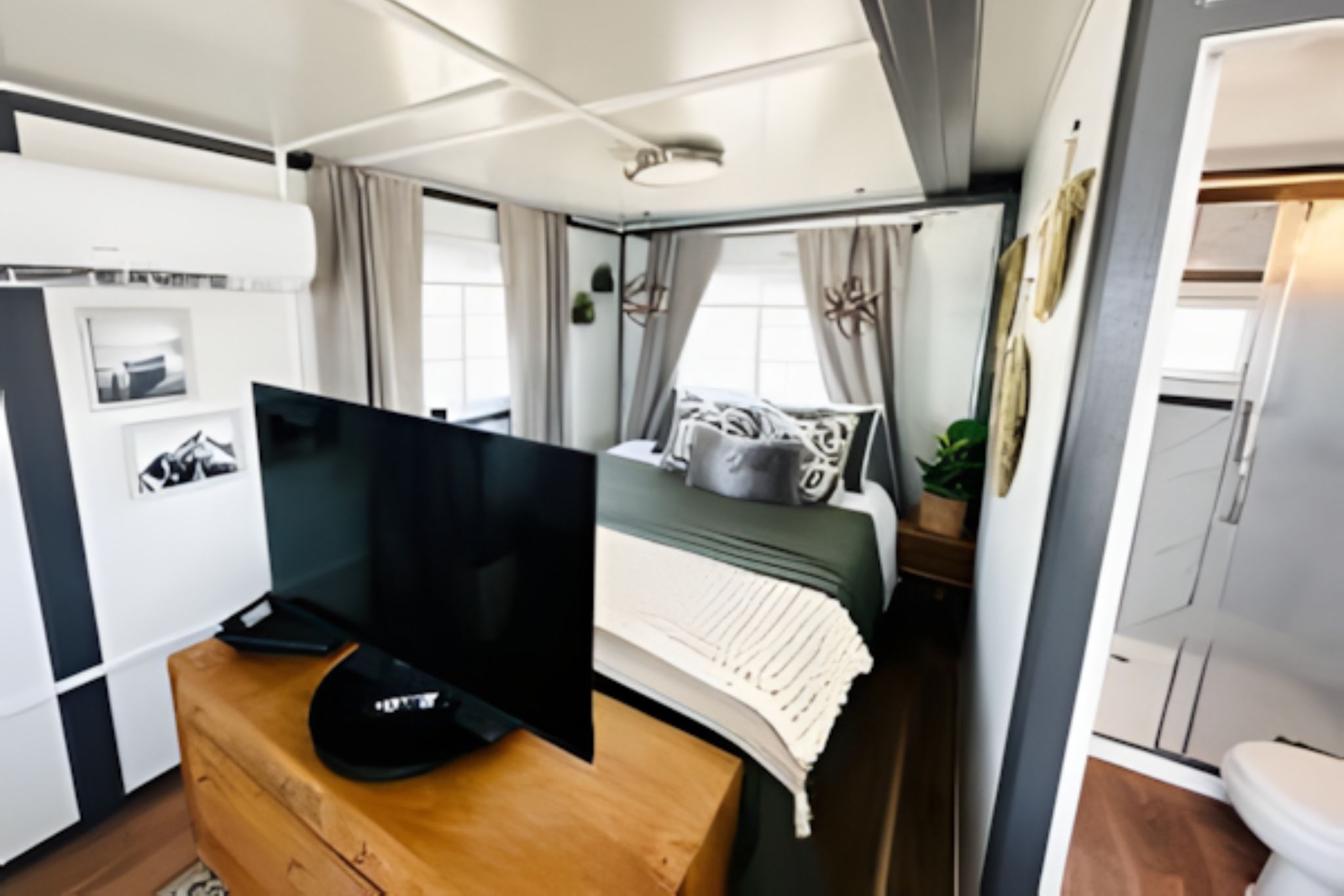A compact living space with a bed, a television, a dresser, and a small kitchenette.