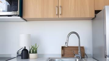 A kitchen with wooden cabinets, a stainless steel sink, a microwave, a potted plant, a lamp, and a basket.