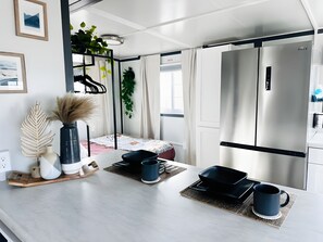 A modern kitchen with a stainless steel refrigerator, a dining area with a table set for two, and a hanging plant. - Private Studio Suite with Queen and Full Beds, Full Kitchen and In-Unit Laundry (Pecos)
