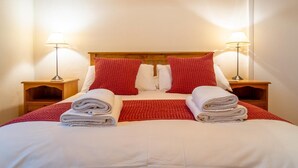 Ein ordentlich bezogenes Bett mit weißer und roter Bettwäsche, zwei Nachttische mit Lampen und ein Holz-Kopfteil.