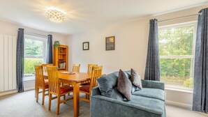 Un salon confortable avec un canapé, une table à manger, des chaises, une bibliothèque et une grande fenêtre avec des rideaux.