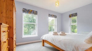Une chambre à coucher avec un lit, deux fenêtres avec des rideaux, une commode et un luminaire.