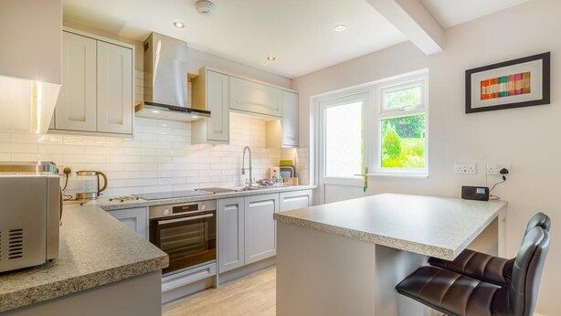 Une cuisine moderne avec des meubles blancs, un four encastré et une fenêtre donnant sur un paysage verdoyant.