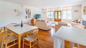 A modern living room with a dining area, wooden flooring, and large windows. - 3 Bed in Ambleside (oc-lr223) (Claife)