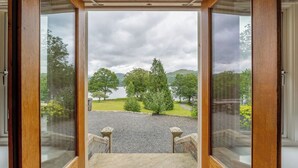 A room with a large window offering a view of a landscaped area with trees and a body of water. - 3 Bed in Ambleside (oc-lr223) (Claife)