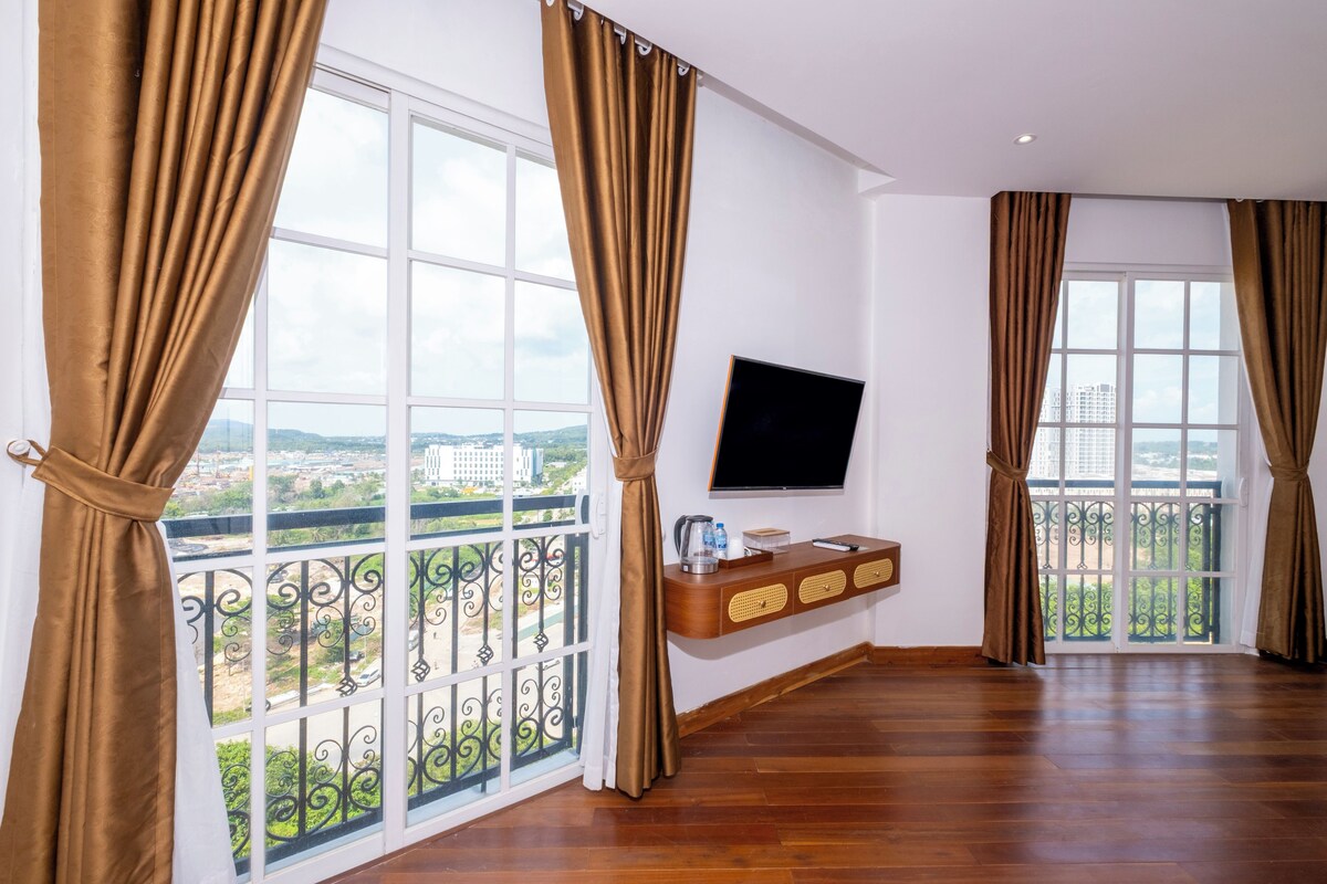 Una habitación amplia con ventanas grandes, un televisor de pantalla plana en la pared y una consola de madera con varios objetos.