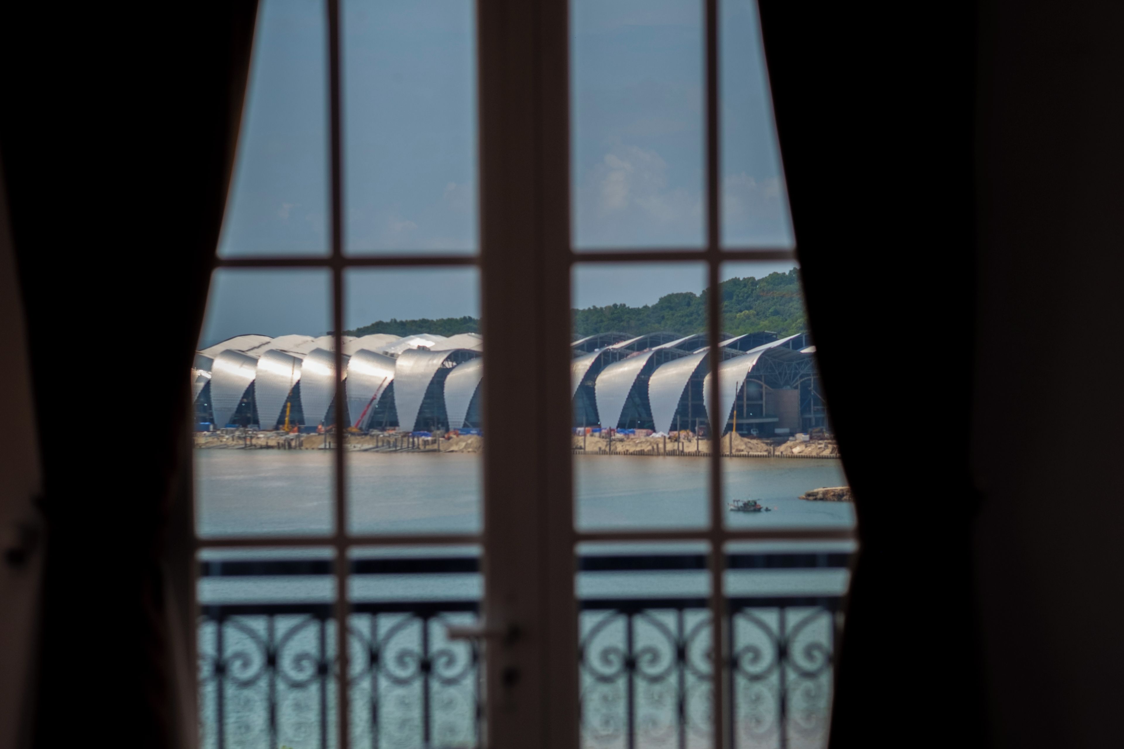 A view through a window with a metal grid, featuring a series of white, curved structures by a body of water.