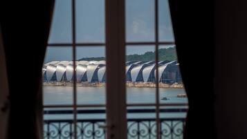 A view through a window with a metal grid, featuring a series of white, curved structures by a body of water.