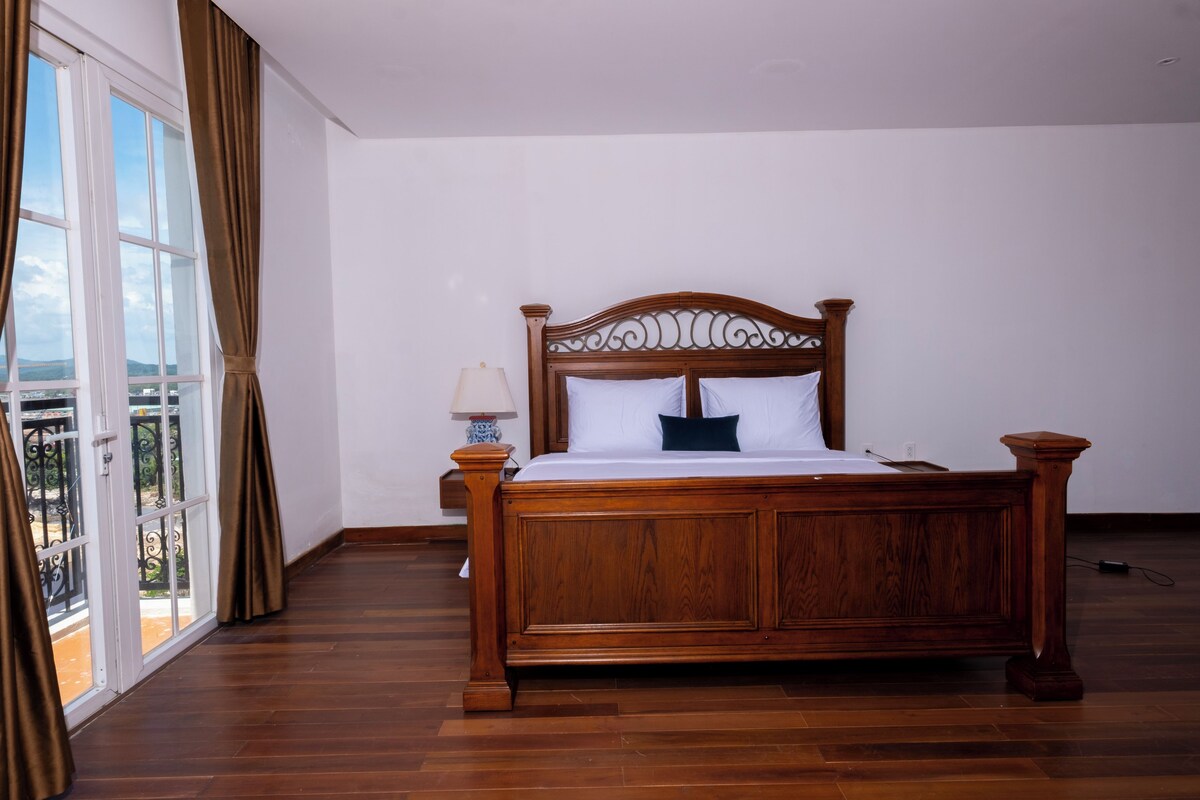 Una cama con dosel de madera con ropa blanca en una habitación con un ventanal y vistas a un balcón.