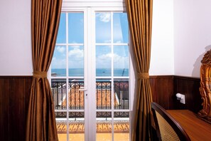 Quarto com vista para o mar através de uma janela com cortinas.