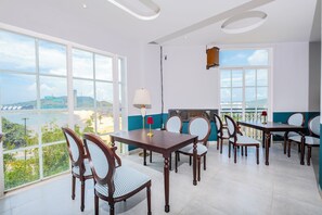 Comedor con vista a la playa y al paisaje urbano, con mobiliario de madera y ventanas amplias.
