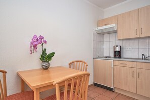 A small kitchen with a wooden table, chairs, a coffee maker, and a potted orchid. - Charmante Ferienwohnung fur 3 mit Balkon im Seepark Sellin (Sellin)