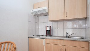 A kitchen with wooden cabinets, a stainless steel sink, a coffee maker, and a white range hood. - Charmante Ferienwohnung fur 3 mit Balkon im Seepark Sellin (Sellin)