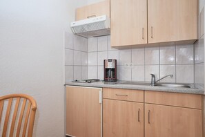 A kitchen with wooden cabinets, a stainless steel sink, a coffee maker, and a white range hood. - Charmante Ferienwohnung fur 3 mit Balkon im Seepark Sellin (Sellin)