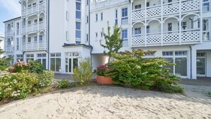 A multi-story building with balconies, a sandy courtyard, and various plants. - Charmante Ferienwohnung fur 3 mit Balkon im Seepark Sellin (Sellin)