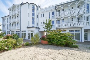 A multi-story building with balconies, a sandy courtyard, and various plants. - Charmante Ferienwohnung fur 3 mit Balkon im Seepark Sellin (Sellin)