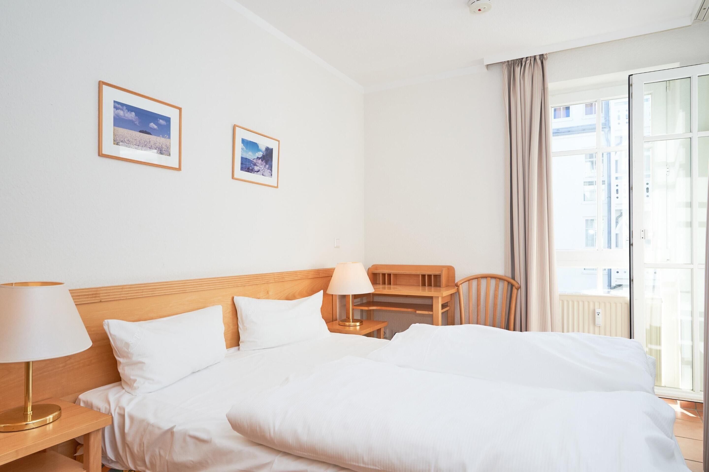 A hotel room with a bed, a desk, a chair, and two framed pictures on the wall.