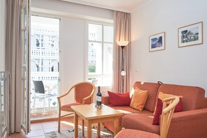 A living room with a sofa, a table, a chair, a bottle of wine, and a lamp. - Charmante Ferienwohnung fur 3 mit Balkon im Seepark Sellin (Sellin)