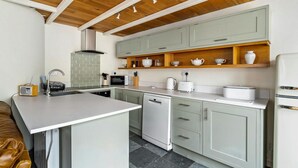 Una cucina con un piano di lavoro bianco, lavastoviglie integrata, forno a microonde, tostapane e frigorifero.