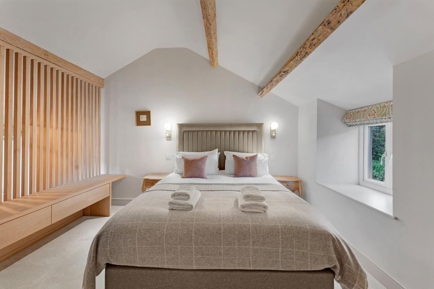 A bedroom with a large bed, wooden slat bench, bedside tables, and a window with a view.