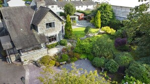 Ein Steinhaus mit geneigtem Dach, ein kleiner Garten mit verschiedenen Pflanzen und ein gepflasterter Auffahrt.
