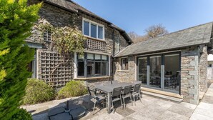 Ein Steinhäuschen mit Terrasse, Tisch und Stühlen sowie einer großen Schiebeglastür.