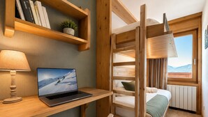 A room with a wooden desk, a laptop, a bed, a window with a view, and a shelf with books and a plant. - Mont-Vallon (Les Allues)