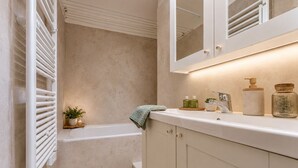 A bathroom with a bathtub, a sink with toiletries, and a mirror above the sink. - Mont-Vallon (Les Allues)