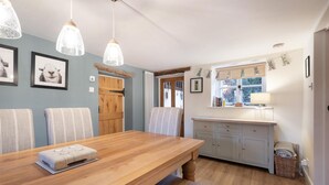 Ein Essbereich mit Holztisch und Stühlen, eine Küche mit Fenster und Pendelleuchten.