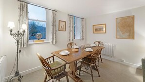 Ein Esszimmer mit Holztisch, vier Stühlen, einem Globus auf der Fensterbank und gerahmten Kunstwerken an den Wänden.