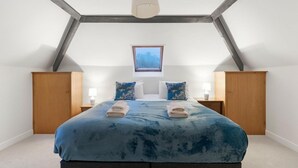 Ein Schlafzimmer mit schrägem Dach, einem Bett mit blauer Bettdecke, zwei Nachttischen mit Lampen und einem Fenster mit Aussicht.