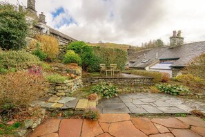 A stone pathway leading to a seating area with a bench, surrounded by lush greenery and stone walls. - 4 Bed in Ambleside (oc-lr082) (Ambleside)