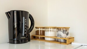 En kaffemaskine i sort står på en hvid bordplade med tre glasbeholdere på en træhylde.