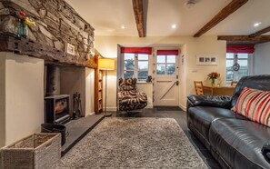 A cozy living room with a stone wall, a fireplace, a leather sofa, and a patterned armchair. - 1 Bed in Ambleside (oc-lr163) (Ambleside)
