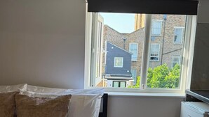 Una camera da letto con un letto, cuscini, un termosifone e una finestra vista edifici.